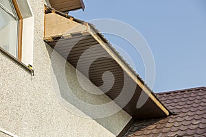 Bottom view detail of new modern house cottage corner with stucco walls, brown shingled roof and unfinished siding installation o