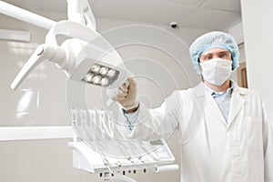Bottom view of a doctor portrait dentist, surgeon in uniform and mask on his face, wearing glasses, holding lamp in her