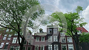 Bottom view footage of historical and traditional buildings, big trees and sky in Amsterdam from canal boat tour.