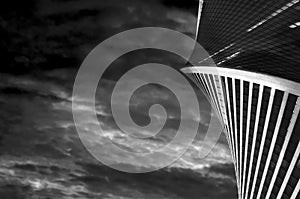 Bottom view of glass skyscraper in shape of spiral on the background of dramatic dark sky with clouds. Black and white shot of