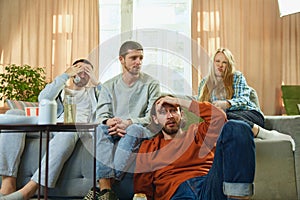 Bottom view of group of friends sitting on sofa in living room and upset about the goal scored against their favorite