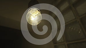 Bottom view of a hanging swaying light bulb inside the entrance of a buiulding. Stock footage. Close up of a blinking