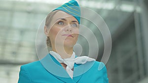 Bottom view of happy beautiful woman in stewardess uniform standing in airport. Close-up of smiling confident Caucasian