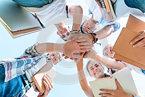 bottom view of happy multiethnic teenage classmates stacking hands in park