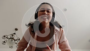 Bottom view of happy young Caucasian woman wearing headphones singing and dancing looking at camera. Party at home