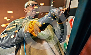 Bottom view horizontal image of adult worker man manufacturing in his workshop. Mature carpenter male grinding with sparks in