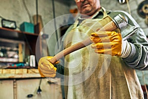 Bottom view image of an adult craftsman manufacturing in his workshop. Professional senior worker man looking to the the hatchet