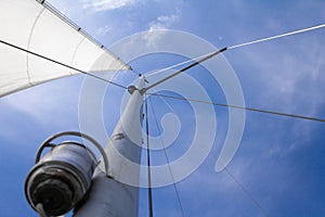 Bottom view of mast and sail of yacht on blue sky background, selective focus