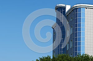 Bottom view of a modern office building and trees against a blue sky background. Summer city landscape.