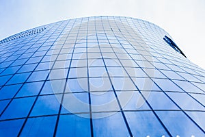 Bottom view of a modern skyscraper with glass window against blue sky.