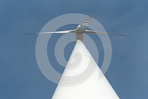 bottom view of a modern windmill against a blue sky. The white blades of the wind turbine. Clean and renewable energy production.