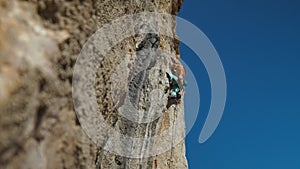 bottom view of muscular strong man rock climber climbs on vertical cliff on rock wall on blue sky background. man puts