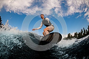 bottom view of one-armed man wakesurfing on the board down the wave