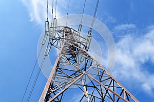 Bottom view of an power pylon and high-voltage wires with glass fuses against a bright blue sky with white clouds on a sunny day.