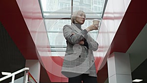 A bottom view slow motion close up shot of a blonde female executive standing inside company`s headquaters and drinking