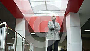 A bottom view slow motion shot of a blonde business woman standing in a hallway of a company's headquaters looking