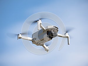Bottom view of a small white drone with camera flying with its propellers out of focus due to speed