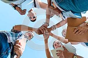 bottom view of smiling multiethnic teenage classmates stacking hands in park