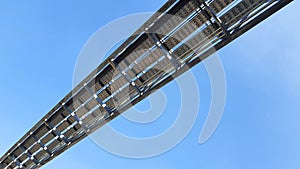 Bottom view of stainless steel electrical or communication cable tray with clear blue sky background.