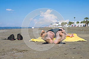 Bottom view on the teen boy feet in the sand lying on yellow towel and sunbathes on the beach.