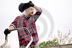 Bottom view of tired man makes a short break while cutting grass with a lawn mower after at backyard of his house