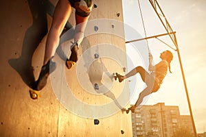 Bottom view of two young climbers practice on artificial climbing wall outdoors. Active sporty women compete on