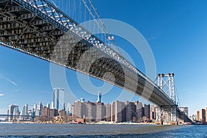 Bottom view of Williamsburg Bridge across the east river during a sunny morning, New York