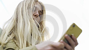 Bottom view of young attractive woman using phone outdoors. Media. Female with long hair typing text message on