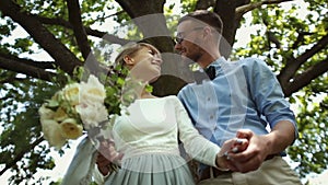 Bottom view. Young beautiful newlyweds kiss against a background of green tree in the park