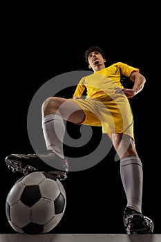 Bottom view of young professional football, soccer player standing with ball isolated on dark background. Concept of