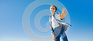 Bottom view of a young smiling attractive woman in jeans clothes at sunny day on the blue sky background.