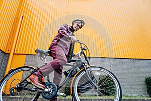 Bottom view Young stylish man in helmet riding on cruiser city Bicycle near orange Wall. Student on the way to college