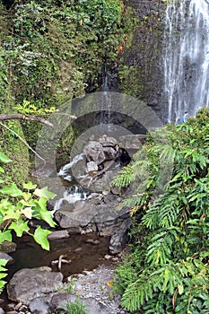 The bottom of Wailua Falls plunging into a stream which flows down a rocky bed in the rainforest on the road to Han