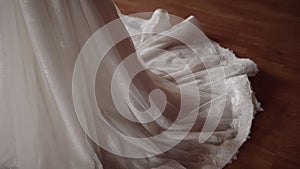 Bottom of white wedding dress with sequins and lace on edge lies on wooden floor