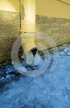 The bottom of a yellow drainpipe with ice