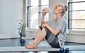 Bottoms up. a mature woman practicing yoga while having a drink of water inside of a studio during the day.
