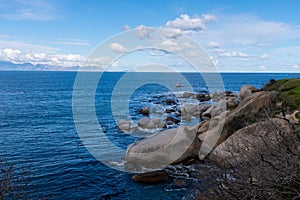 Boulders in blue ocean with view across bay.