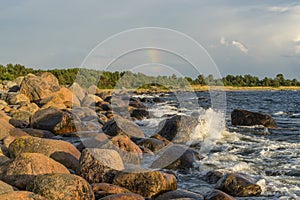 Boulders, forest, shore, evening light, sunset, clouds, blue sky and rainbow on the Baltic Sea