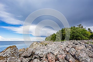 Boulders, forest, shore, evening light, sunset, clouds, blue sky and rainbow on the Baltic Sea.