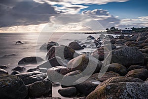 Boulders, forest, shore, evening light, sunset, clouds, blue sky and rainbow on the Baltic Sea.