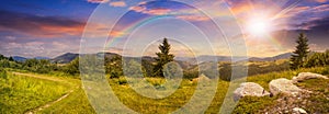 Boulders on hillside meadow in mountain at sunset with rainbow