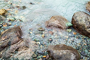 Boulders and pebbles on the bank of a river with milky green colour water