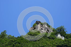 Boulders surrounded by green trees on the mountain with blue sky background