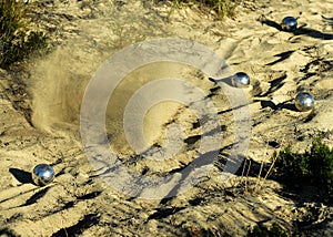 A Boules metal ball disappearing in a sand spray