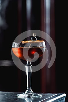 The Boulevardier Cocktail with orange chips on top. On a bar desk