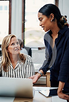 Bouncing ideas off of one another. an attractive businesswoman helping a female colleague in the office.