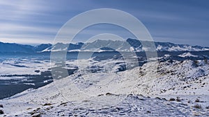 Boundless expanses are visible from a snow-covered high-altitude plateau.