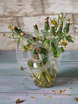 Bouquet of answered dandelions in a glass jug on a turquoise plank tray, side view from close range