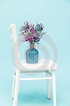 Bouquet of artificial lavender bouquet flowers in glass vase on white chair and blue background. Minimal style interior. Copy