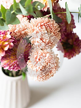 Bouquet of autumn flowers in a vase on the table. Peach asters and burgundy with yellow dahlias with eucalyptus branches in a vase